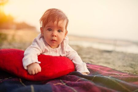 baby lies on plaid and read pillow in park with beautiful sunset on the backgroundの写真素材