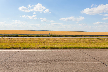 Summer adventure road with old asphalt, gold rye field, blue cloudy sky Background