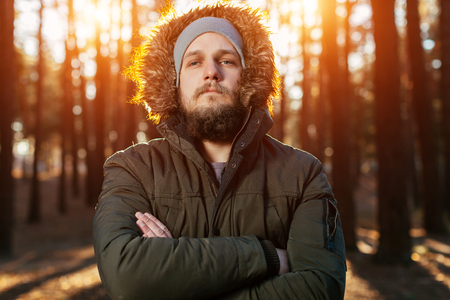 portrait of serious bearded hipster man with mustache in the woods forest. dressed in the green parka with artificial fur on the hoodの写真素材