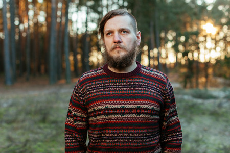 bearded hipster with a mustache in the forest. portrait of a man in a red sweater with a beautiful ornamentの写真素材