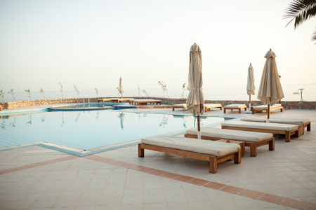 Swimming pool with chaise lounge and sunshade at tropical resort Summer eveningのeditorial素材