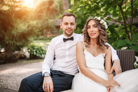 the bride and groom sitting on a chair with arms around each otherの写真素材