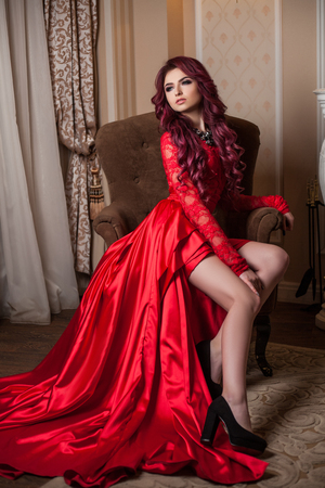 redheaded passion young woman in a red dress in the Interiorの写真素材