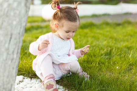 little curly girl with two tails sitting on the lawn near a tree. Summer season photo. Playful mood. Sunnyの写真素材