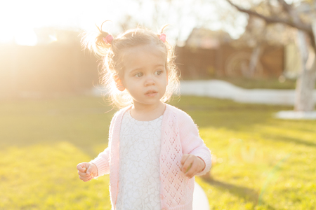 soft focus photo of a little curly girl with two tails walking in the backyard on the green grass Dressed in a pink blouse in the hands of the grapes...の写真素材