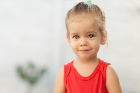 Close up Portrait of blonde girl with blue eyes in the park. Child, baby girl close up smile. Dressed in red blouseの写真素材