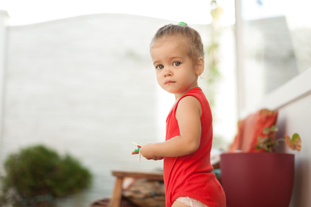 Close up Portrait of blonde girl with blue eyes in the park. Child, baby girl close up smile. Dressed in red blouseの写真素材