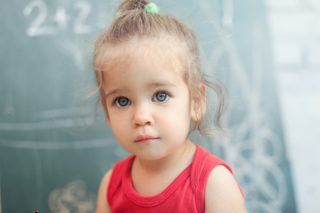 happy school girl on math classes in kindergarten finding solution and solving problems Close up portrait of cute girl with blackboard with mathematics on the backgroundの写真素材