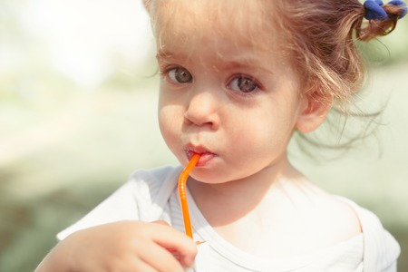 Sunny close up portrait of a little child drinking from a straw juiceon blurred summer background. Health eating conceptの写真素材