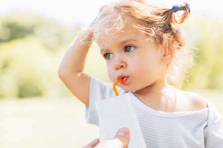 Sunny close up portrait of a little child drinking from a straw juiceon blurred summer background. Health eating conceptの写真素材