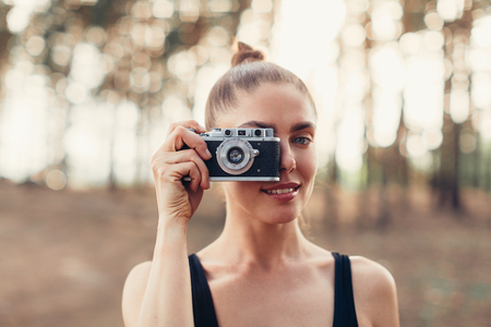 Hipster girl with using vintage photo camera close up, copy space of blank empty mockup, view tourist holding in hands and photograph on device travel on background pine forestの写真素材