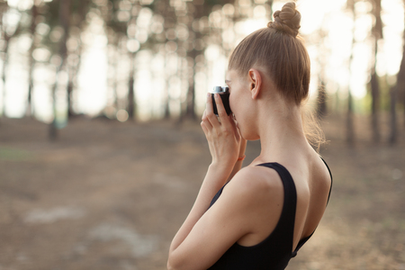 Hipster girl with using vintage photo camera close up, copy space of blank empty mockup, view tourist holding in hands and photograph on device travel on background pine forestの写真素材