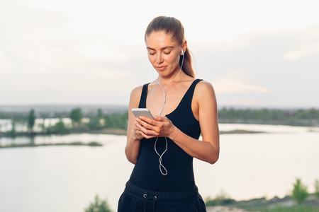 fitness girl with a smartphone on nature background, enjoys sports training, workout Modern sport life conceptの写真素材