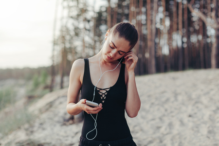 fitness girl with a smartphone on nature background, enjoys sports training, workout Modern sport life conceptの写真素材