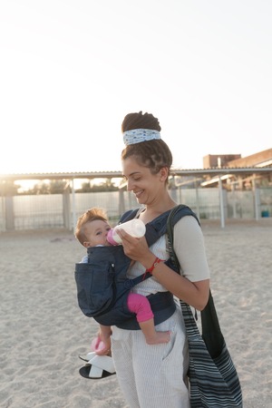 a small child sits in a backpack and walks along with the mother along the seashore. Summer family...