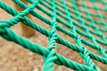 Rope mesh with blurry background. It is a green rope mesh in a playground. It is not a brand new rope mesh but it is old and deteriorateの写真素材