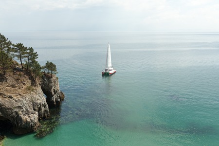Panoramic view of Pacific Ocean blue transparent water, a white sport modern luxury yacht sail boat floating and a green shore with forest, hills. Holiday by the water and sail race. Crozon, France 29 May 2018の写真素材