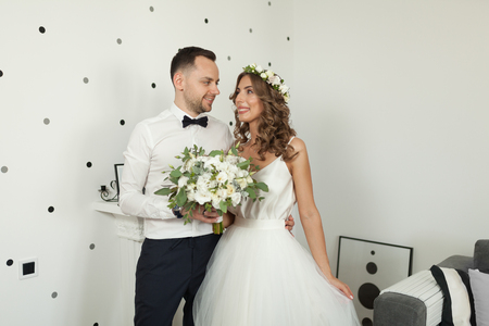 Meeting the bride and groom in the bedroom, the newlyweds are happy. Man dressed in the wgite shirt and bowtie woman dressed in the whitw wedding dress and wreath hairstyle with bouquet in hand.の写真素材