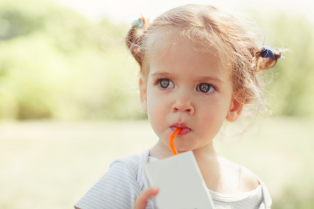 Sunny close up portrait of a little child drinking from a straw juiceon blurred summer background. Health eating conceptの写真素材