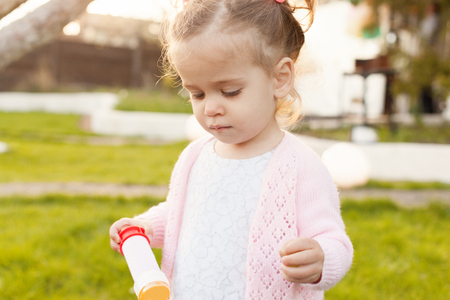a little curly girl with two tails walking in the backyard on the green grass Dressed in a pink blouse in the hands of soap bubblesの写真素材