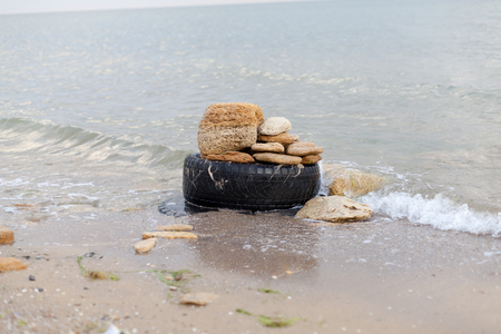 Old black rubber tire left on a beach, environment pollution concept, selective focus, color toned picture.の写真素材