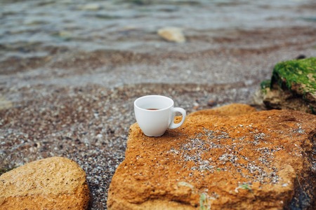 cup of coffee on the sea water and stone background. Sea freshness morning concept.の写真素材