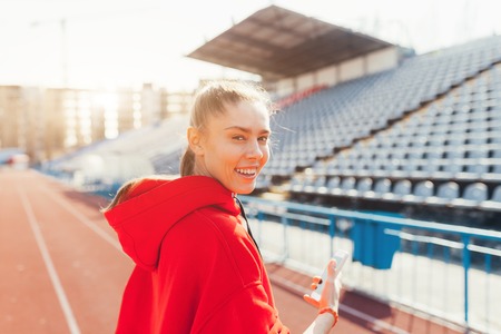 Beautiful lady runner in warm clothes on the stadium looking aside. Wearing red hood. Casual sport wear concept.の写真素材