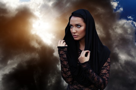 A woman is a prophet sorcerer and a preacher in a black mystical cloak with a hood against a dramatic backgroundの写真素材