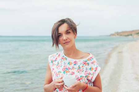 Beautiful woman with short haircut relax during exotic vacation on the beach enjoying sweet coffee or teaの写真素材