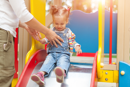 Happy young mother with her baby girl playing in colorful playground for kids. Mom with toddler having fun at summer park. Baby play. Summer family leisure.の写真素材