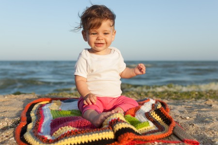 Happy baby smiling and waving hand, sitting on white sandy tropical beach on the carpet Family vacationの写真素材