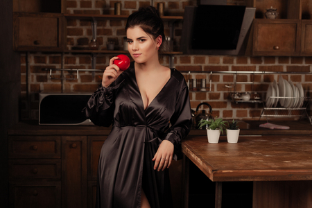 Pretty woman in her kitchen eat red appleの写真素材