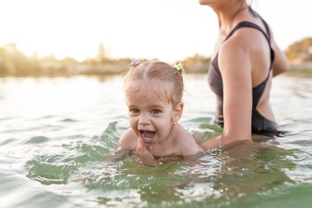 a young unrecognizable mother holding a little baby girl who learns to swim. Concept of summer family vacation. Holiday with the family.の写真素材
