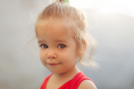Close up Portrait of blonde girl with blue eyes in the park. Child, baby girl close up smile. Dressed in red blouseの写真素材