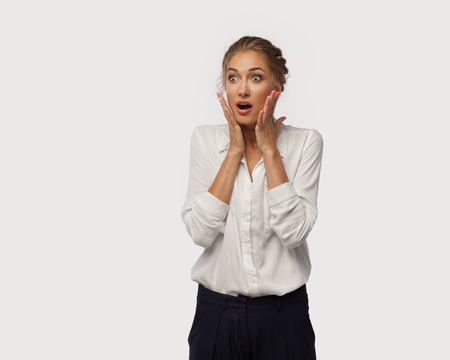 A very surprised business lady dressed in classic office clothes brought her hands to her face. Surprise from sales.の写真素材