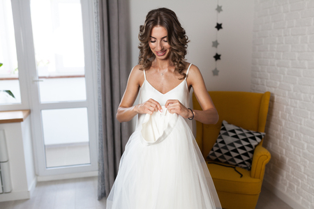 A beautiful curly-haired girl, a future bride measuring a wedding dress in her house before the weddingの写真素材