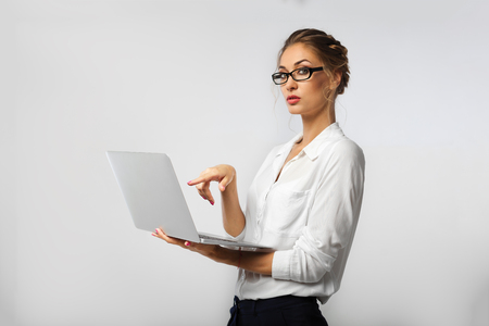 A strict business lady in glasses and co-ordinate office clothes is holding a laptop in her hands and demonstratively pointing at him with her finger.の写真素材