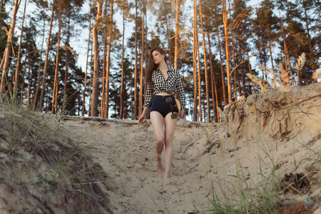 A beautiful girl with a longboard in her hands in nature in a pine forest in search of a good road that would ride. Concept of youth modern lifestyle.の写真素材