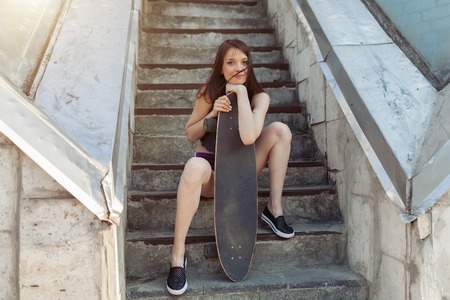 Beautiful young girl with a long board in the city. The concept of modern youth. Active fun holidayの写真素材