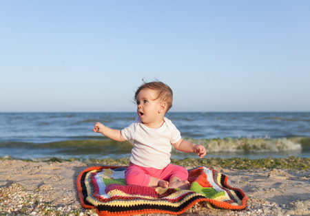 Happy baby smiling and waving hand, sitting on white sandy tropical beach on the carpet Family vacationの写真素材