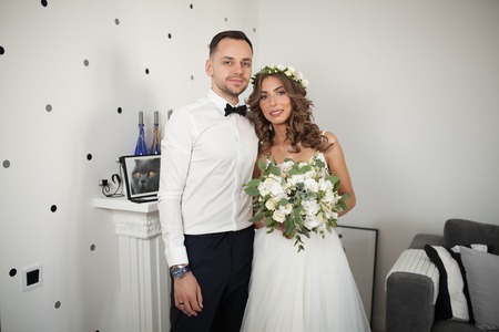 Meeting the bride and groom in the bedroom, the newlyweds are happy. Man dressed in the wgite shirt and bowtie woman dressed in the whitw wedding dress and wreath hairstyle with bouquet in hand.の写真素材