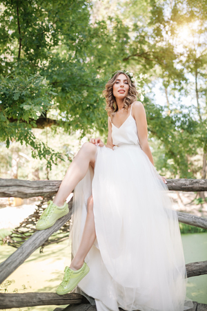 beautiful girl in white dress with a wreath of flowers on her head is standing outdoor in the park with green leaf on the background.の写真素材