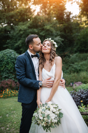 groom dressed in a stylish suit kissing with her beautiful bride in a white wedding dress in nature Wedding outdoor ceremony.の写真素材