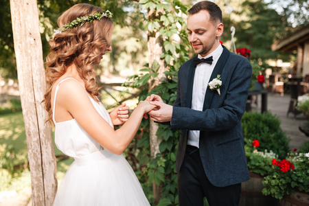 Beauty bride and handsome groom are wearing rings each other. Wedding couple on the marriage ceremony. Beautiful model girl in white dress. Man in suit. Female and male portrait. Cute lady and guy.の写真素材