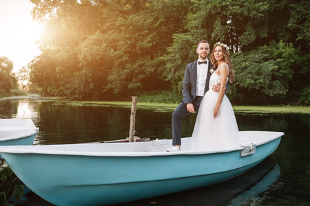 Beautiful couple groom and bride near river boat. Against the background of beautiful nature and sunset.の写真素材