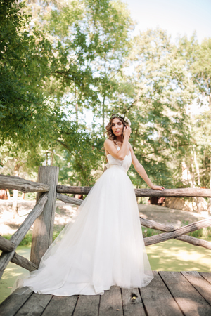 A cute curly woman in a white wedding dress with a wedding bouquet and wreath in her hair standing back to the camera in nature. Concept escaped bride. Forward to a happy bright future Runaway.の写真素材