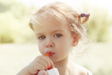 Smiling girl with funny pigtails like Pippi drinks fresh orange juice With blured nature backgroundの写真素材