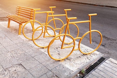 Empty bicycle parking city park with yellow bench on the background.
