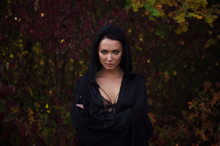 Young woman in the black cloak with a hood in the autumn forestの写真素材
