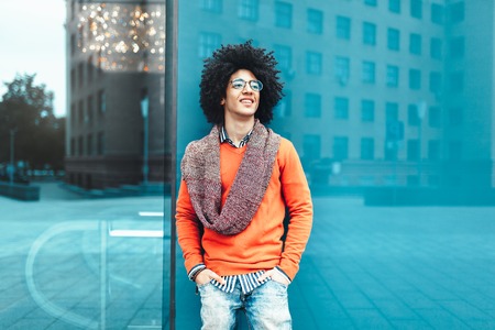 Young fashionable dressed curly black African American with glasses walks through the streets against a skyscraper. A student standing against the background of glass wallsの写真素材
